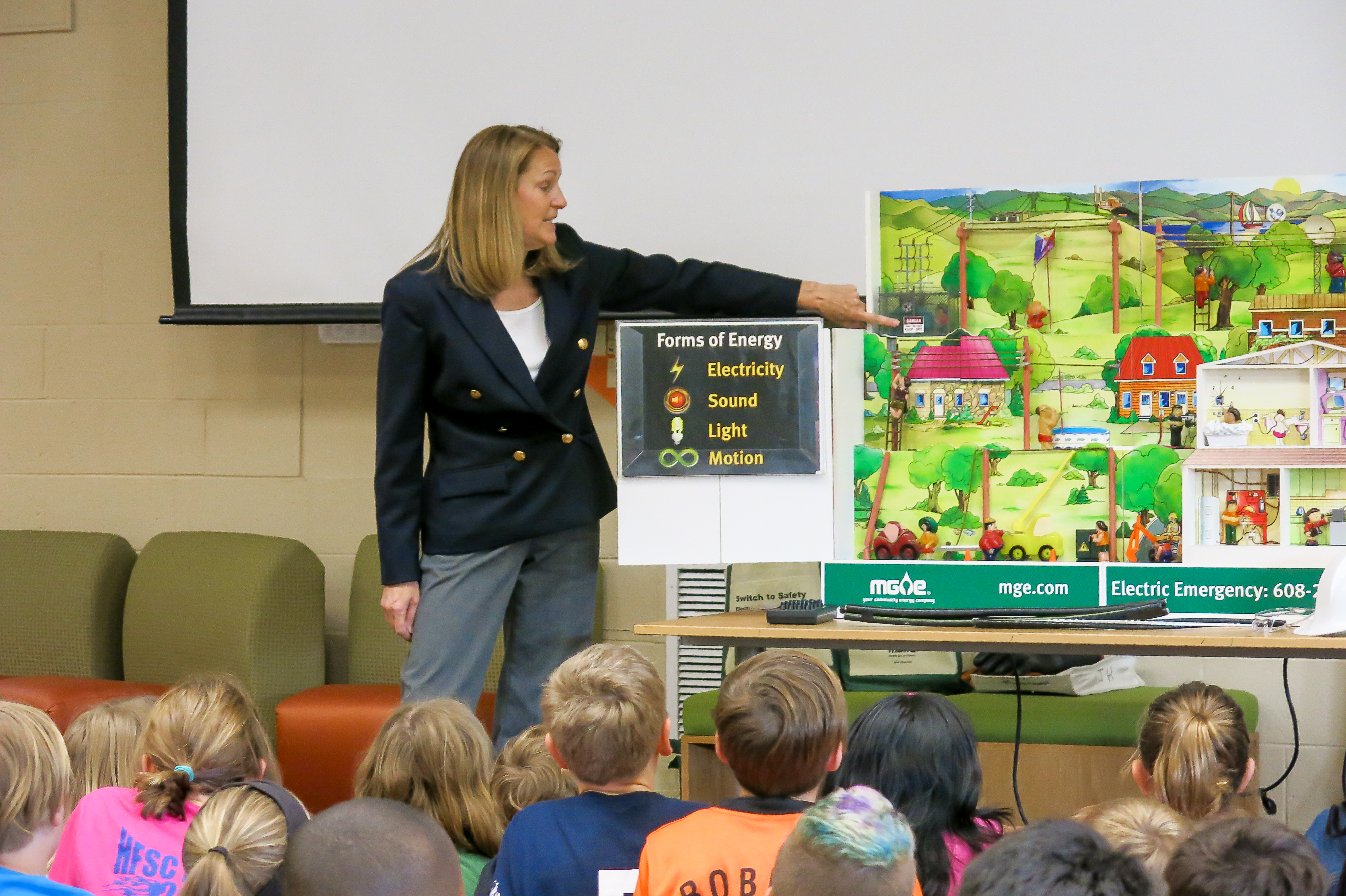 Flossie points to Hazard Hamlet, an energized tabletop city, explaining electric safety scenarios to a group of students.