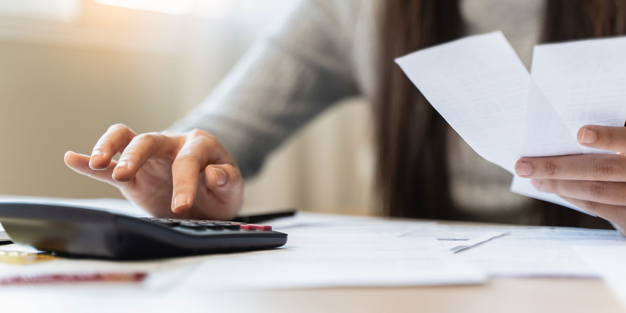 Person paying bills at home desk with calculator, receipts in hand.