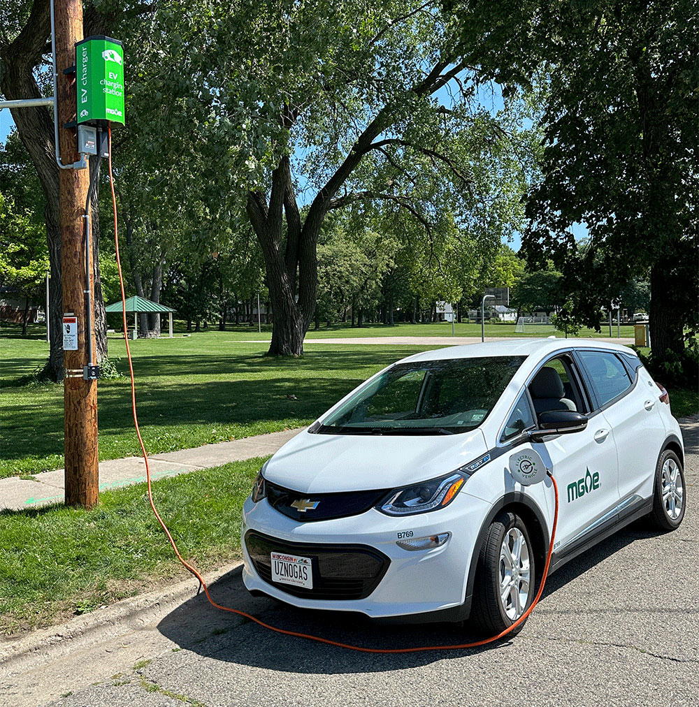 A white electric vehicle charging at one of MGE's pole-mounted charging stations.