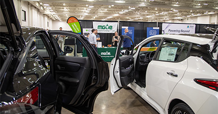 Four employees at the MGE booth at the Transportation & Innovation Expo with two electric vehicles in the foreground.