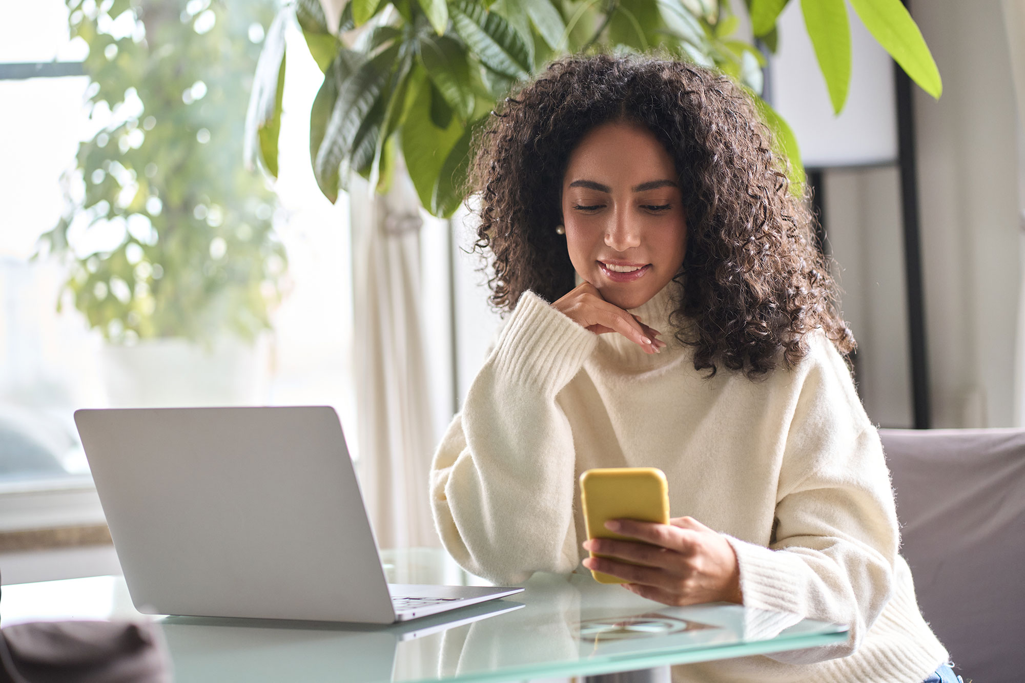 Woman using laptop and phone to manage bills.