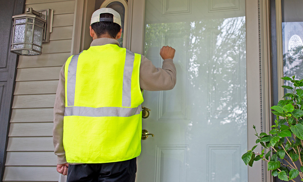 Man wearing safety vest knocking at front door