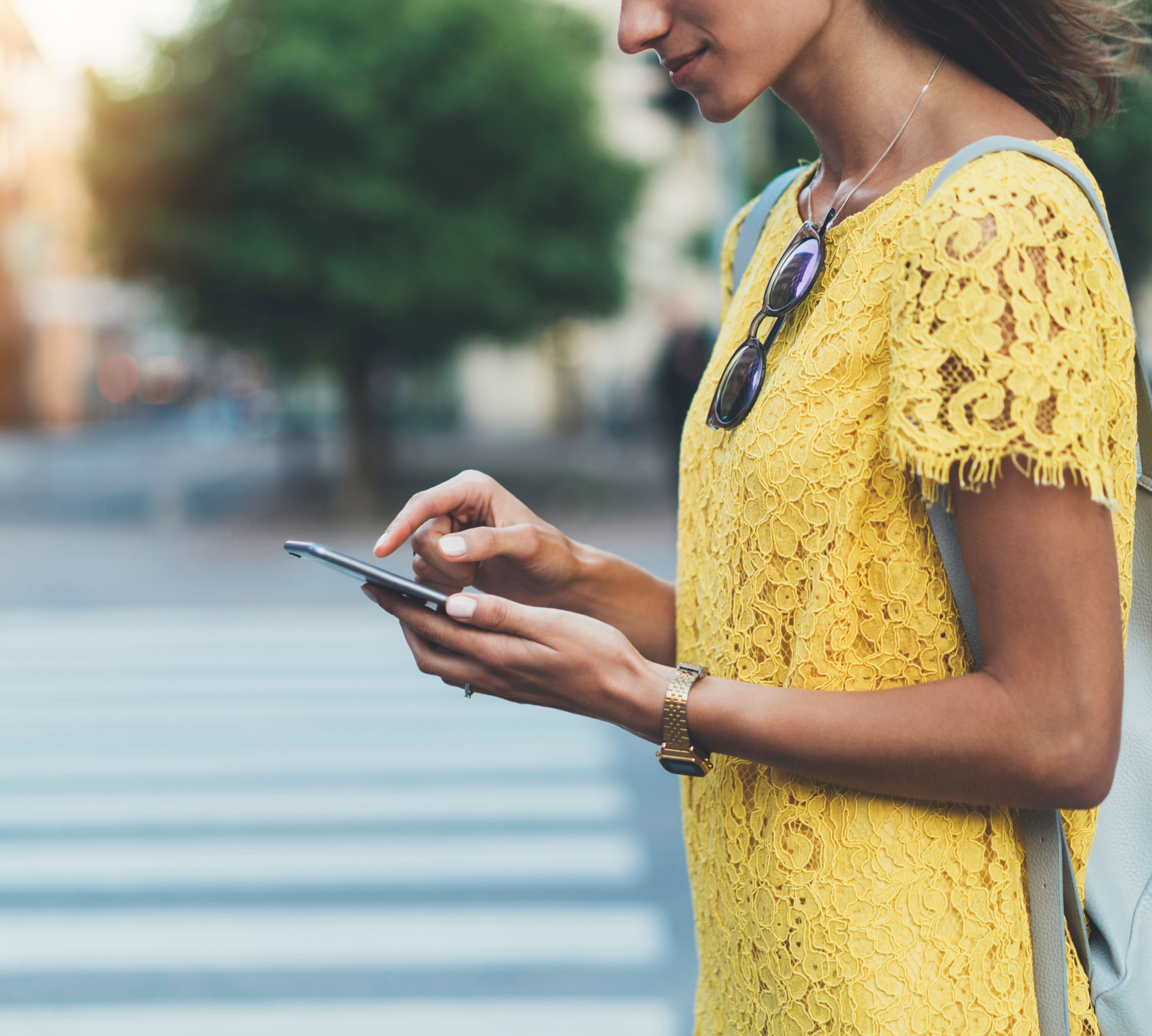 Woman wearing a yellow short sleeve blouse standing outside, dialing on her mobile phone.