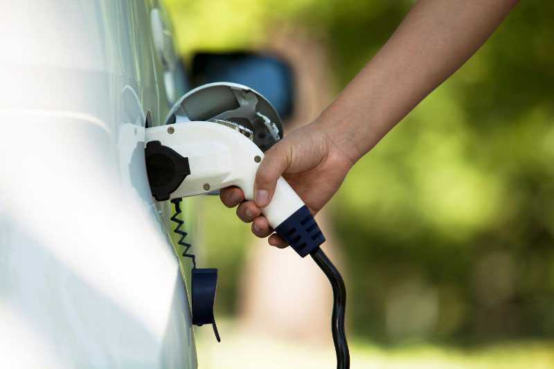 Close-up of a person's hand on an electric vehicle charger plugged into a charging station.