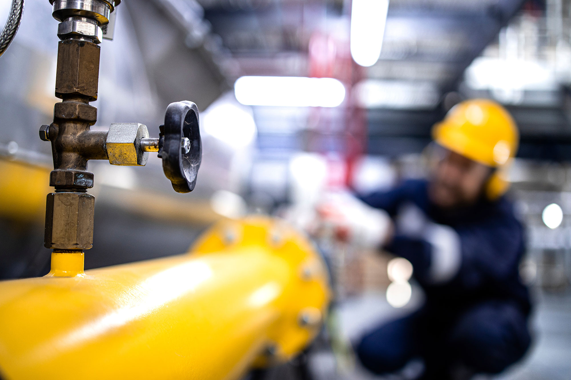 Close up view of natural gas pipeline with valve and worker working in the background.