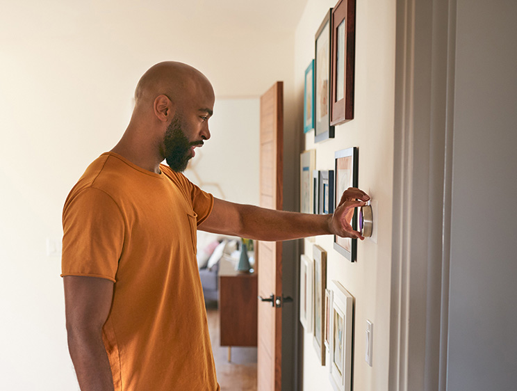 African American man adjusting a smart thermostat on the wall in his home.