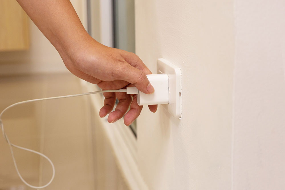 Unplugging a white device power cord from a wall outlet.