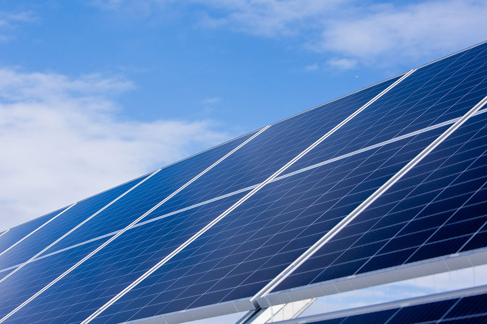 A closeup of a tilted solar panel with blue sky and clouds in the background.