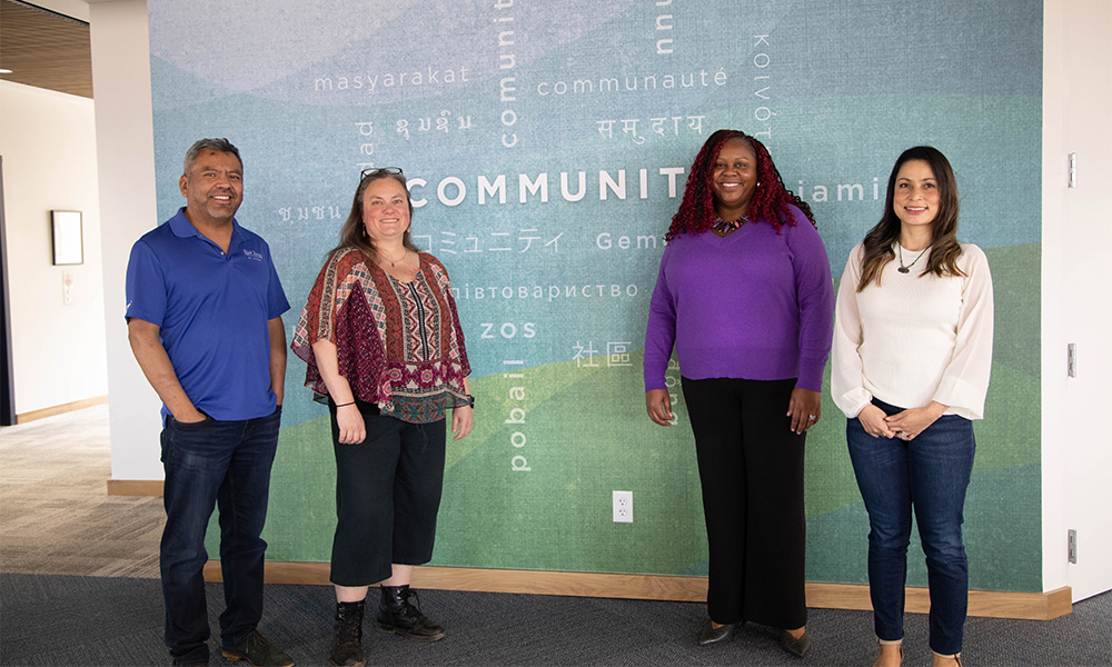 Members of the MGE School Partnerships team standing in front of a wall that says community.