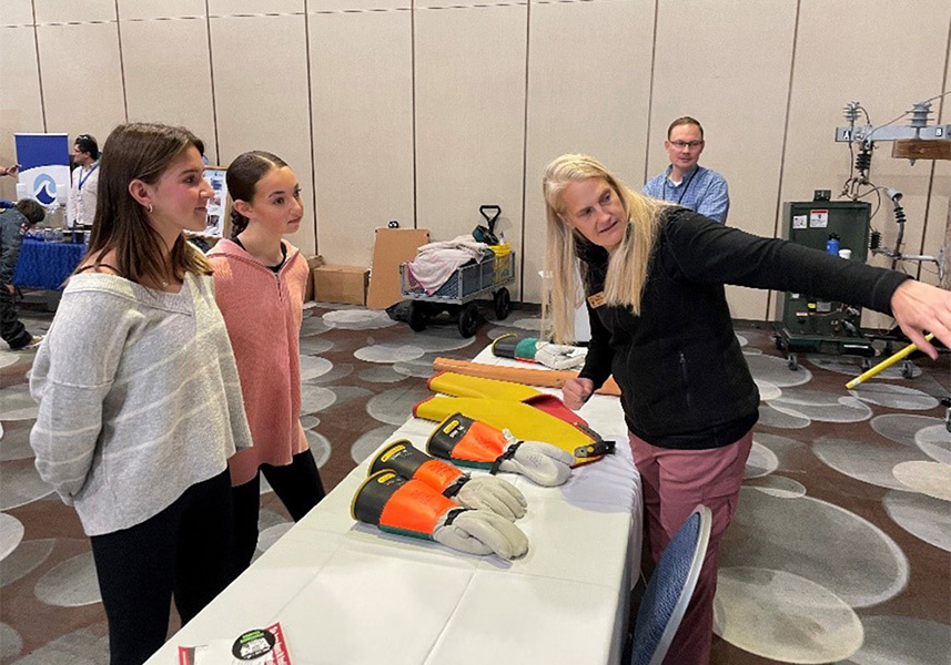 A woman talks to two female students as she points. There's a table with gloves in between them.