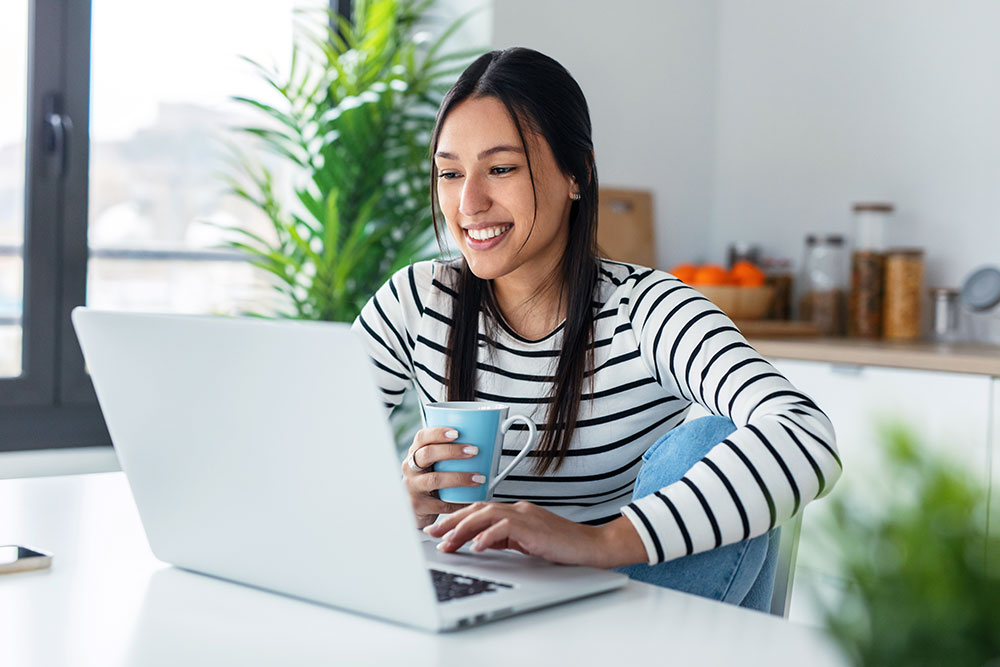 Woman sitting at table while paying bills on laptop