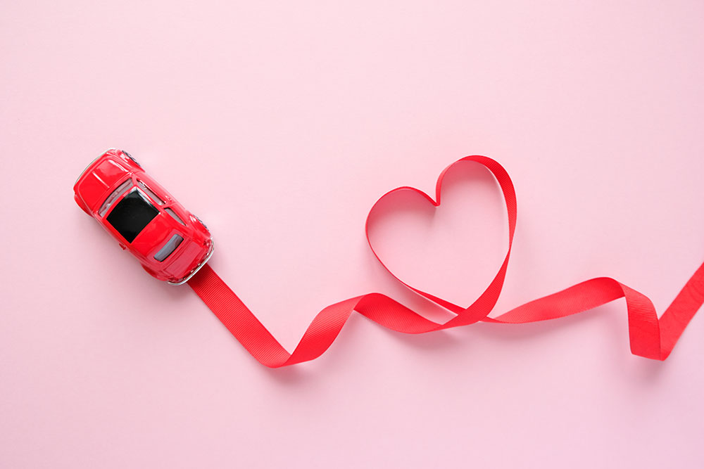 Red ribbon curled into a heart shape with a red  toy car