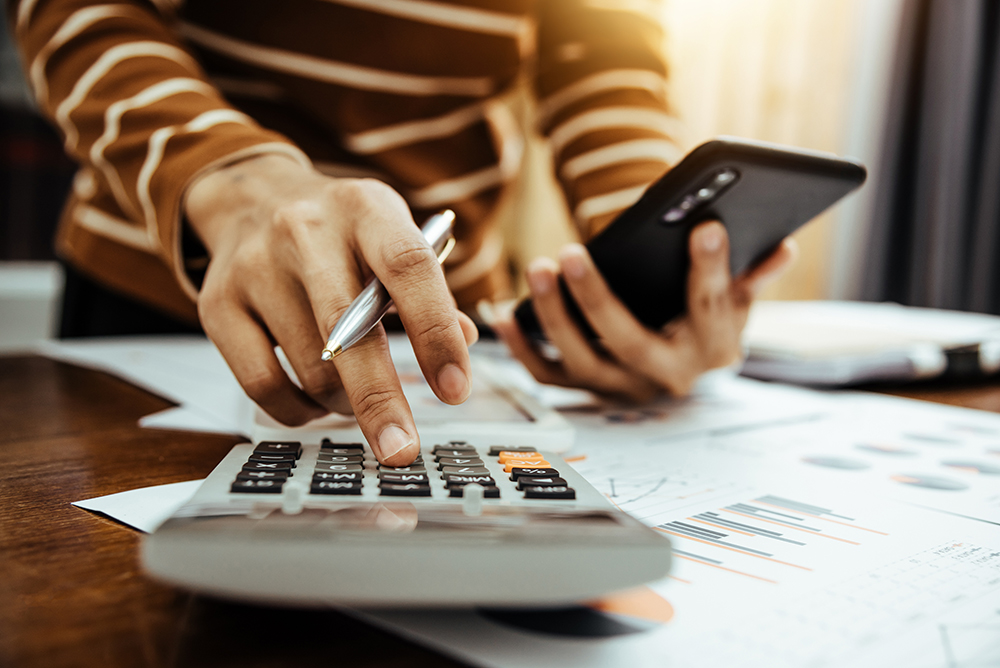 person using calculator and phone to manage finances.
