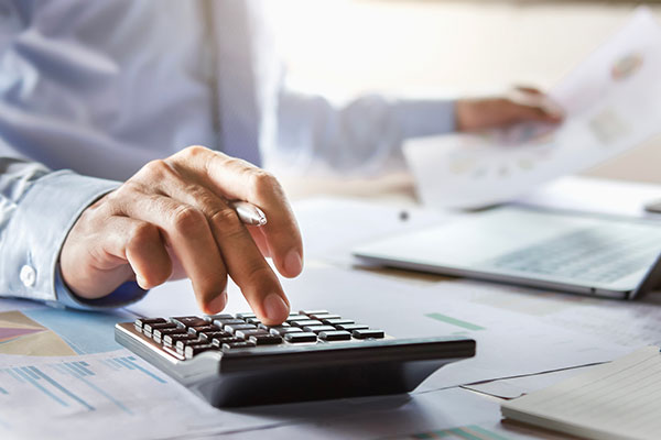 A closeup of a man at a desk with a calculator, bill and lap top.