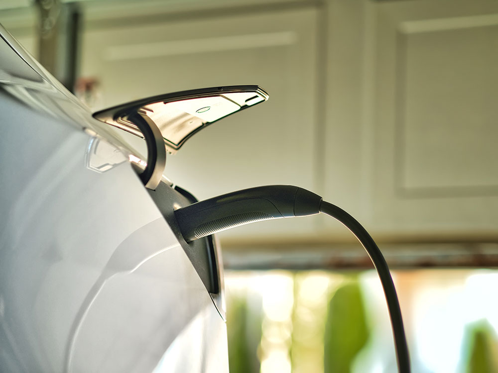 close-up of a white electric vehicle connected to a charger in a garage