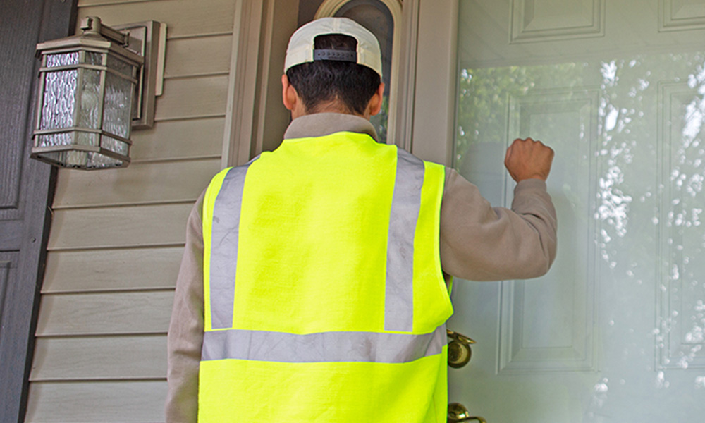 Utility worker with safety vest knocking on a door