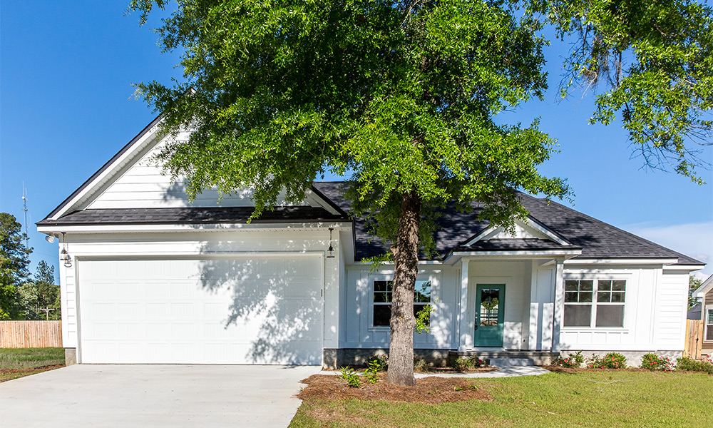 Una casa blanca de dos pisos sombreada por un frondoso árbol verde.