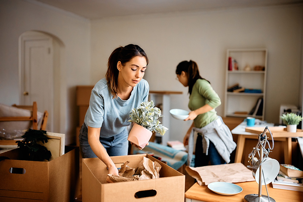 Two women packing up household items in their apartment.
