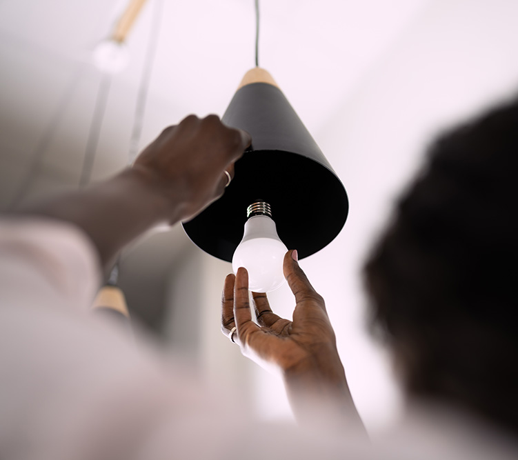 Person replacing an an LED bulb in a black, pendant-style light fixture.
