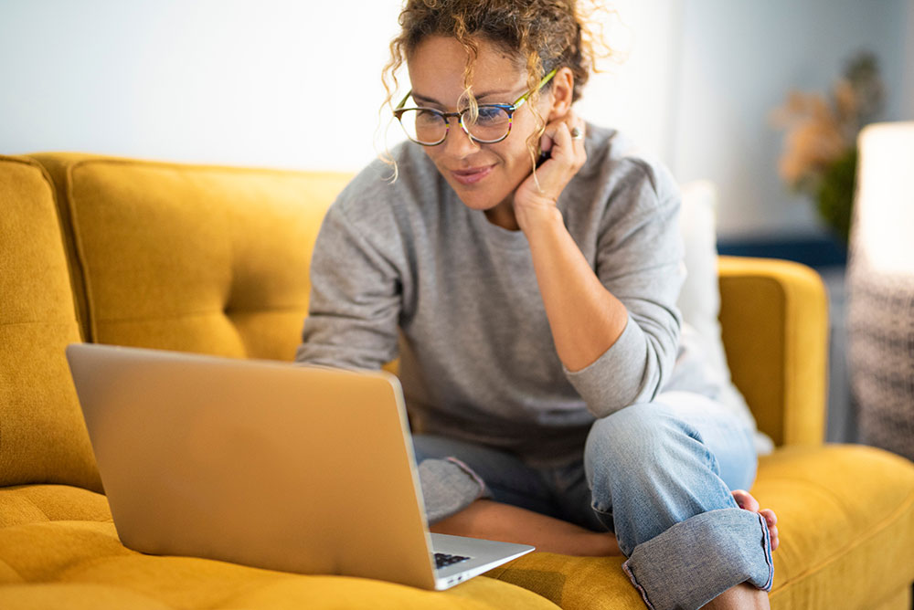 Woman using laptop while sitting on gold couch.